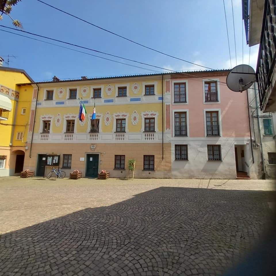 Un edificio color pastello con bandiere esposte. Di fronte, una piazza acciottolata.