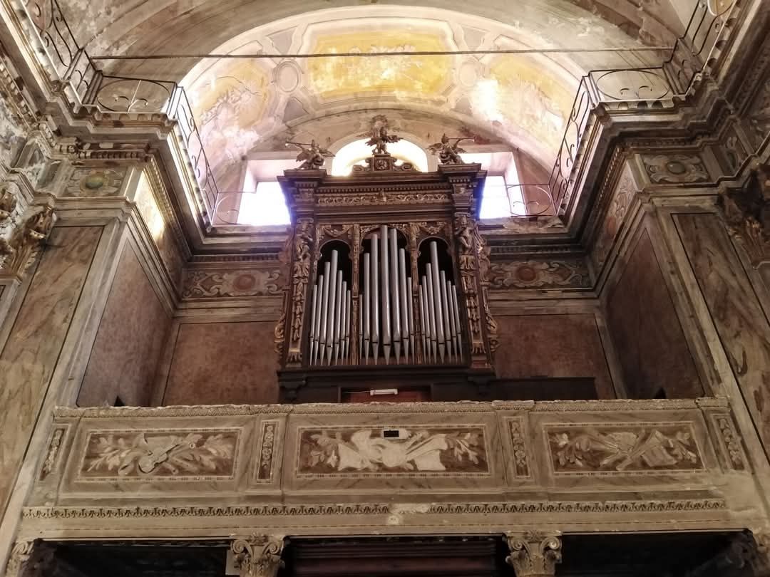 Interno della chiesa con un organo sopra un balcone decorato. Il soffitto è a volta e le pareti sono dipinte.