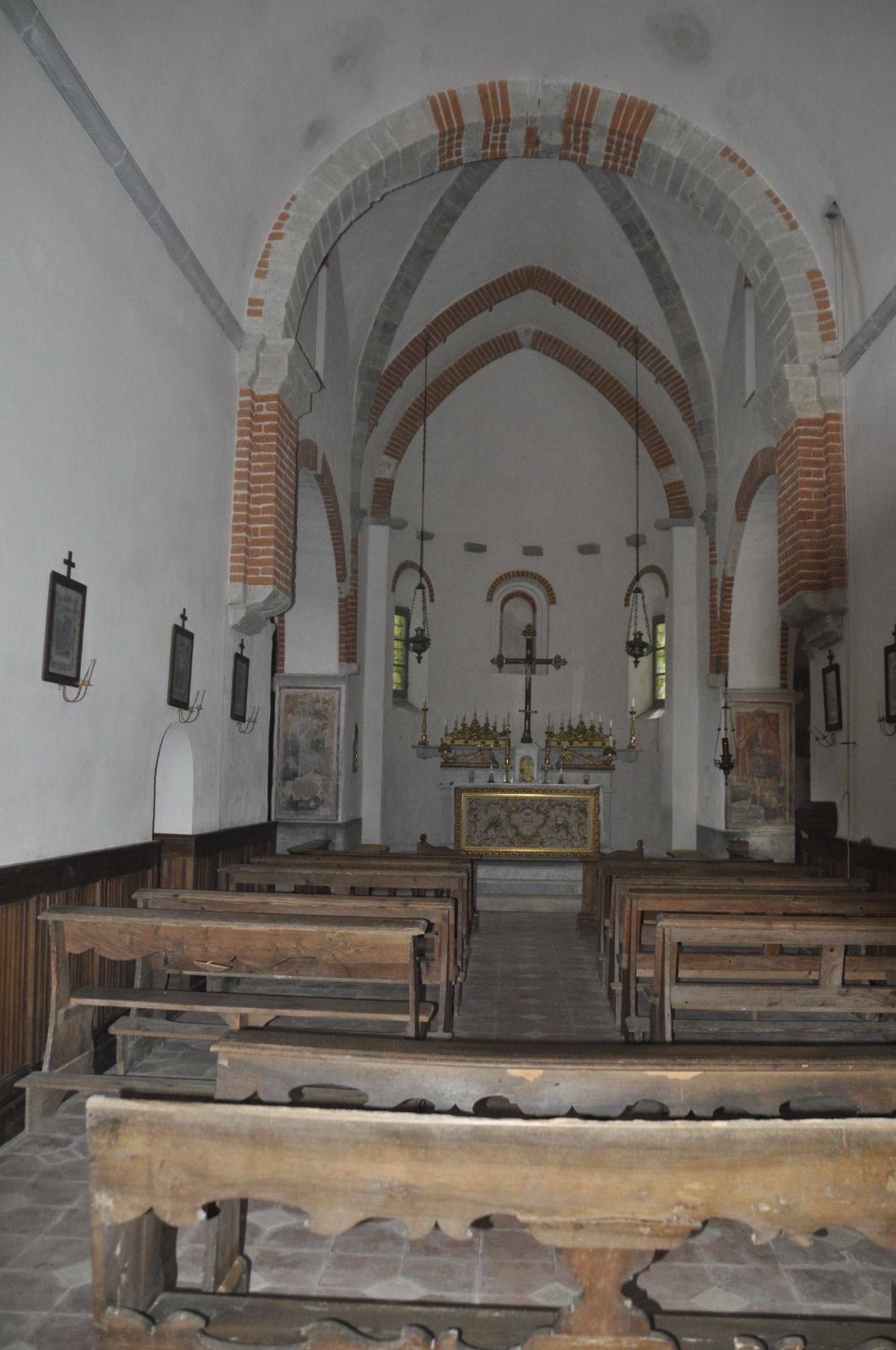 Interno di una chiesa con banchi di legno, soffitto a volta con dettagli in mattoni e un altare centrale.