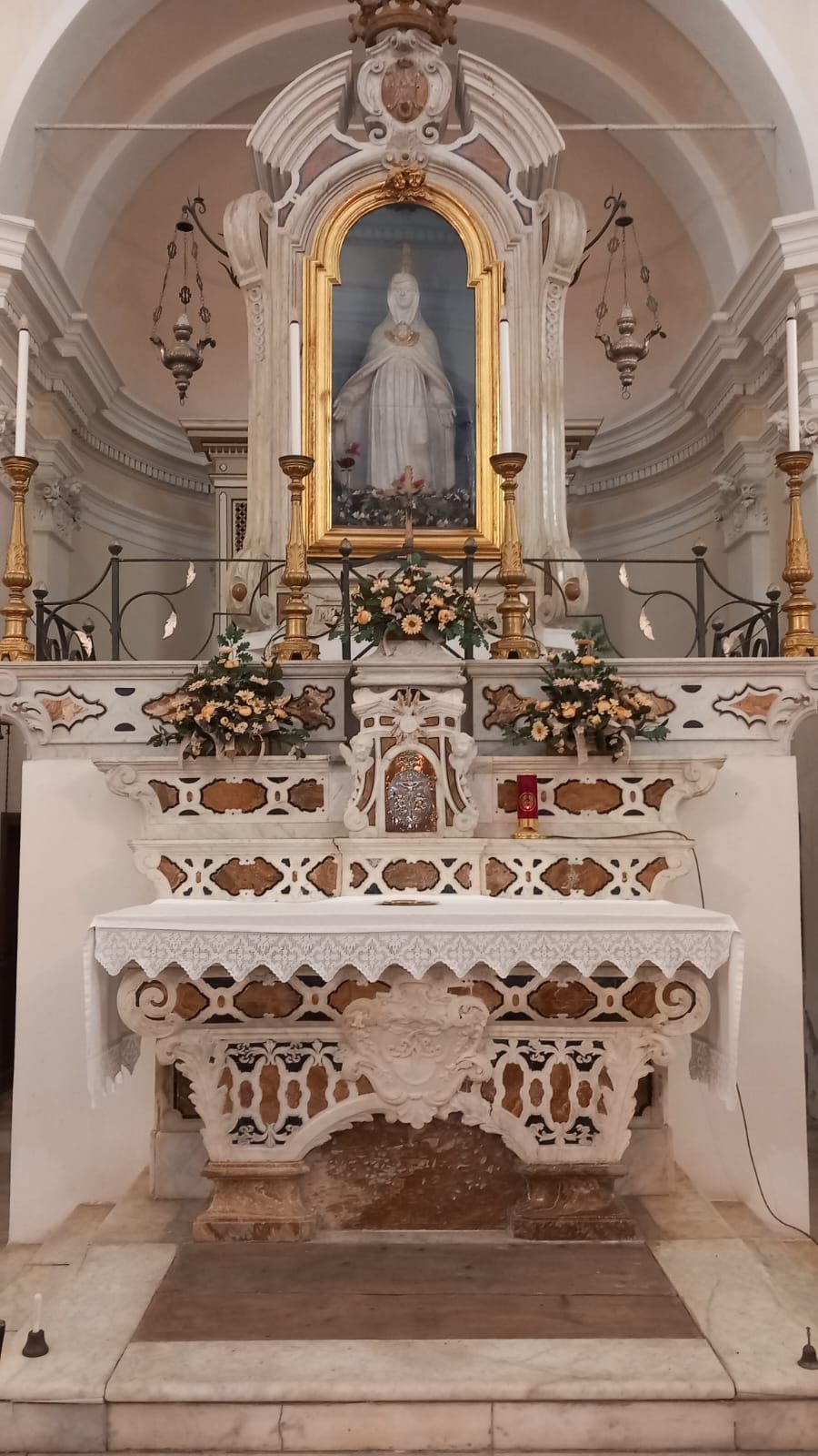 Interno di una chiesa con un altare decorato, composizioni floreali e una statua raffigurante una figura.
