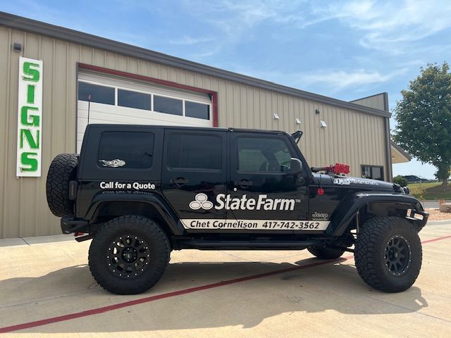 A black jeep with state farm written on the side is parked in front of a building