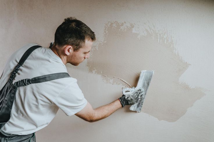 Person plastering a beige wall with a trowel, smoothing fresh paint or plaster.