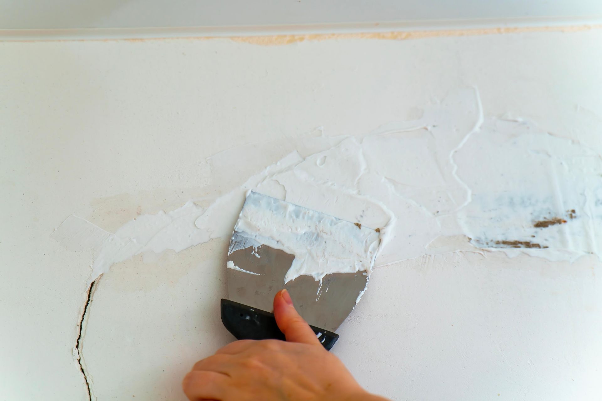 Hand spreading white spackle over a damaged white wall with a putty knife