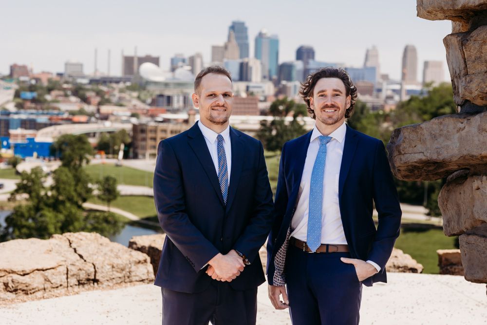 Two men in navy suits standing outdoors with a city skyline in the background