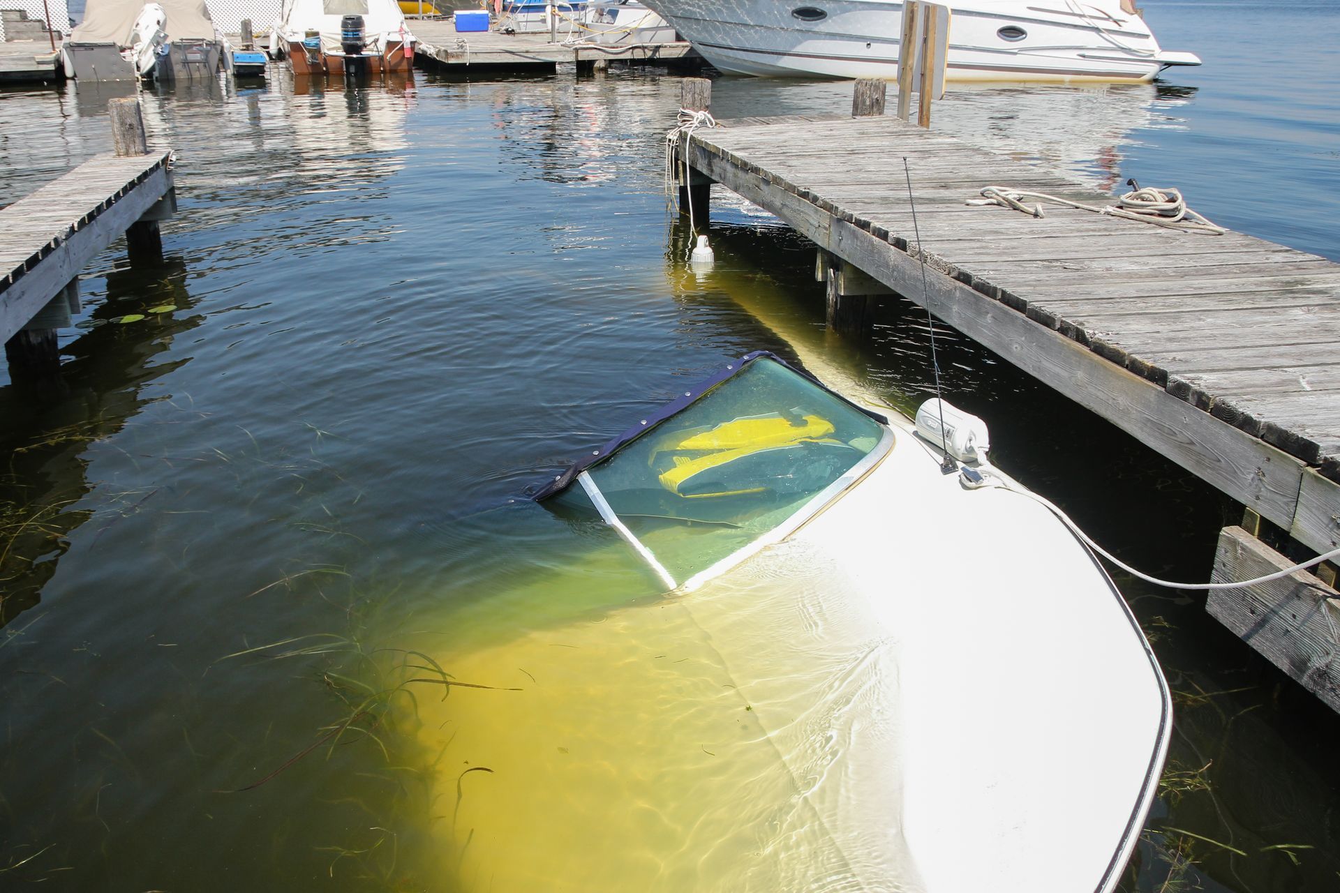 Partially submerged white and yellow sailboat in a marina canal, with docked boats in the background