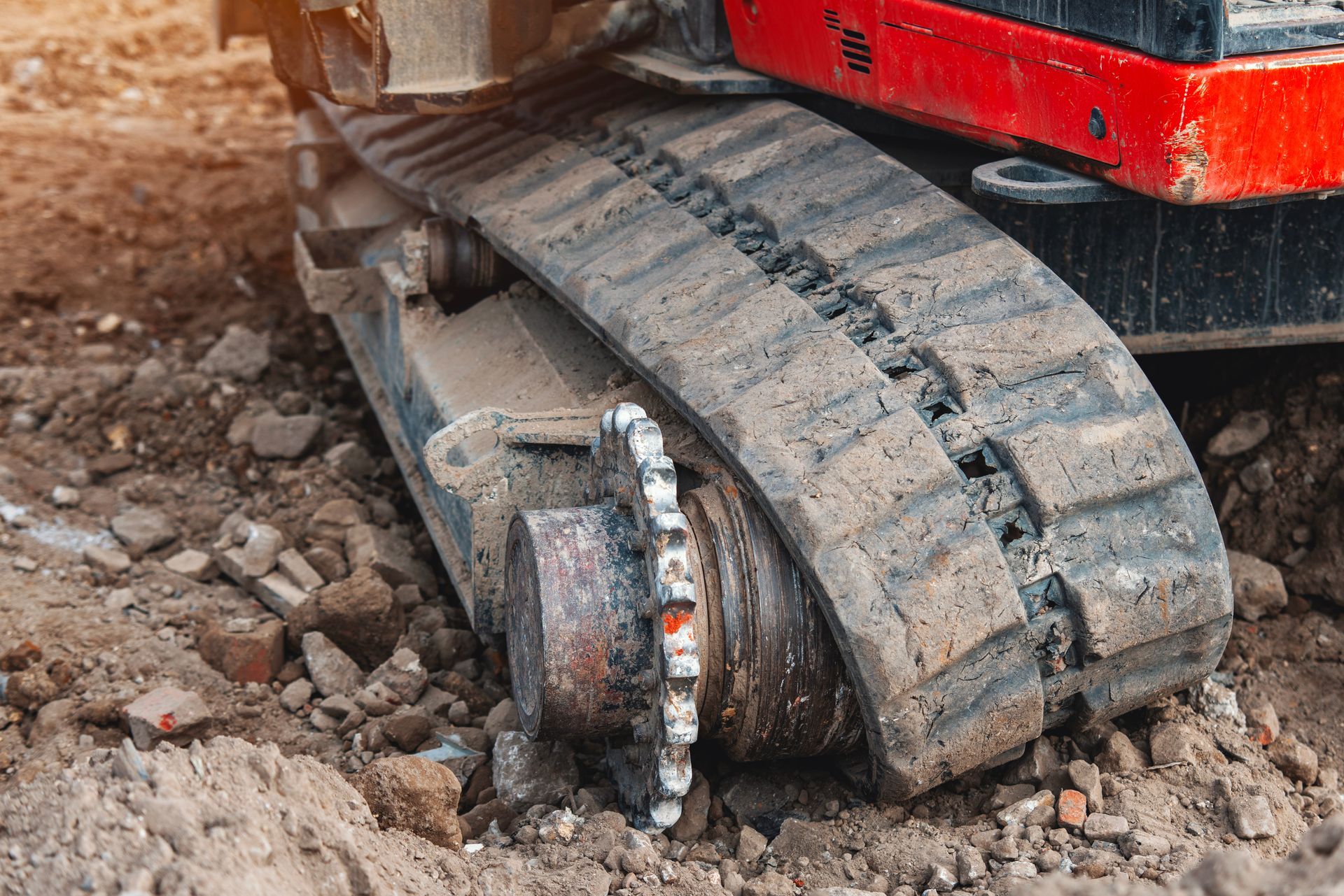 Close-up of a damaged excavator track grinding into rocky ground, with a broken wheel assembly.