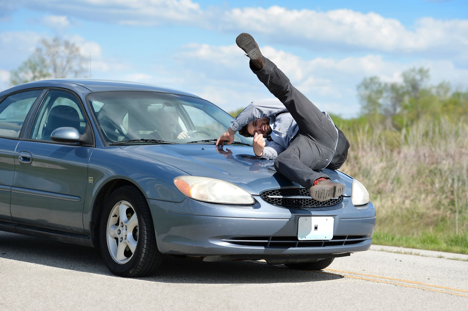 Person doing a handstand on the hood of a blue car on a roadside