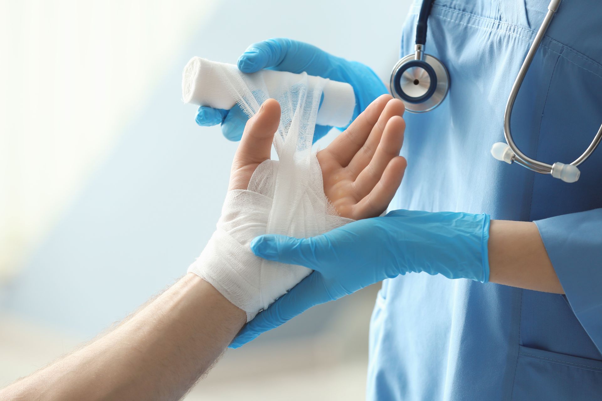 Healthcare worker bandaging a patient’s hand with white gauze and blue gloves