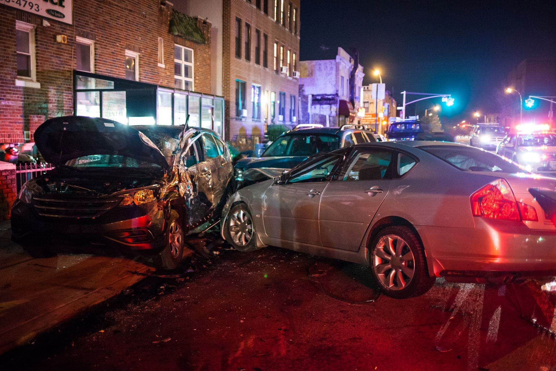 Two damaged cars after a nighttime crash on a city street, with police lights flashing nearby