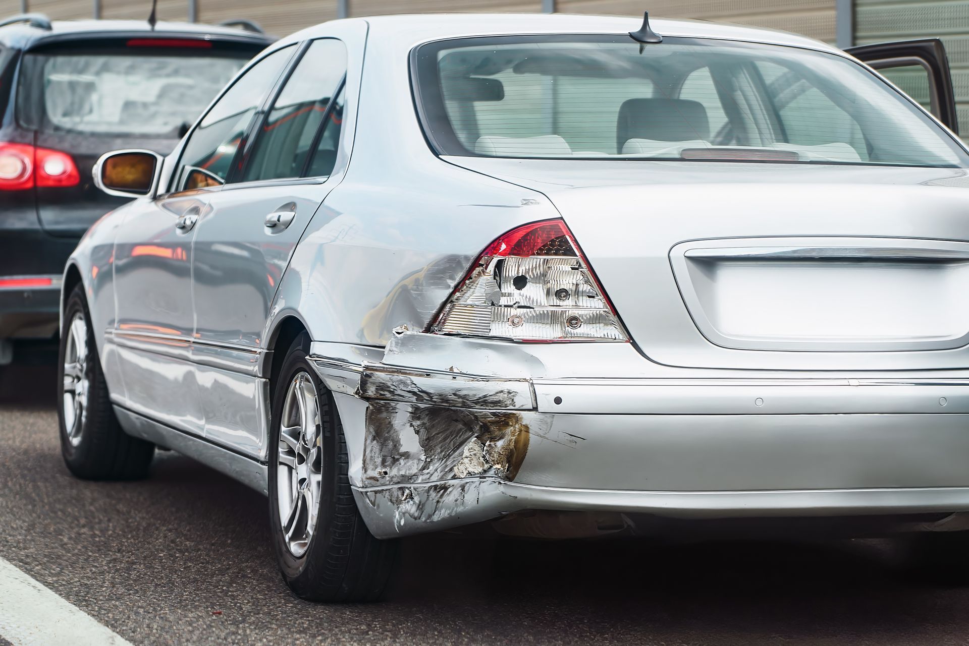 Silver sedan with rear-left side damage from a collision on a road with other cars nearby
