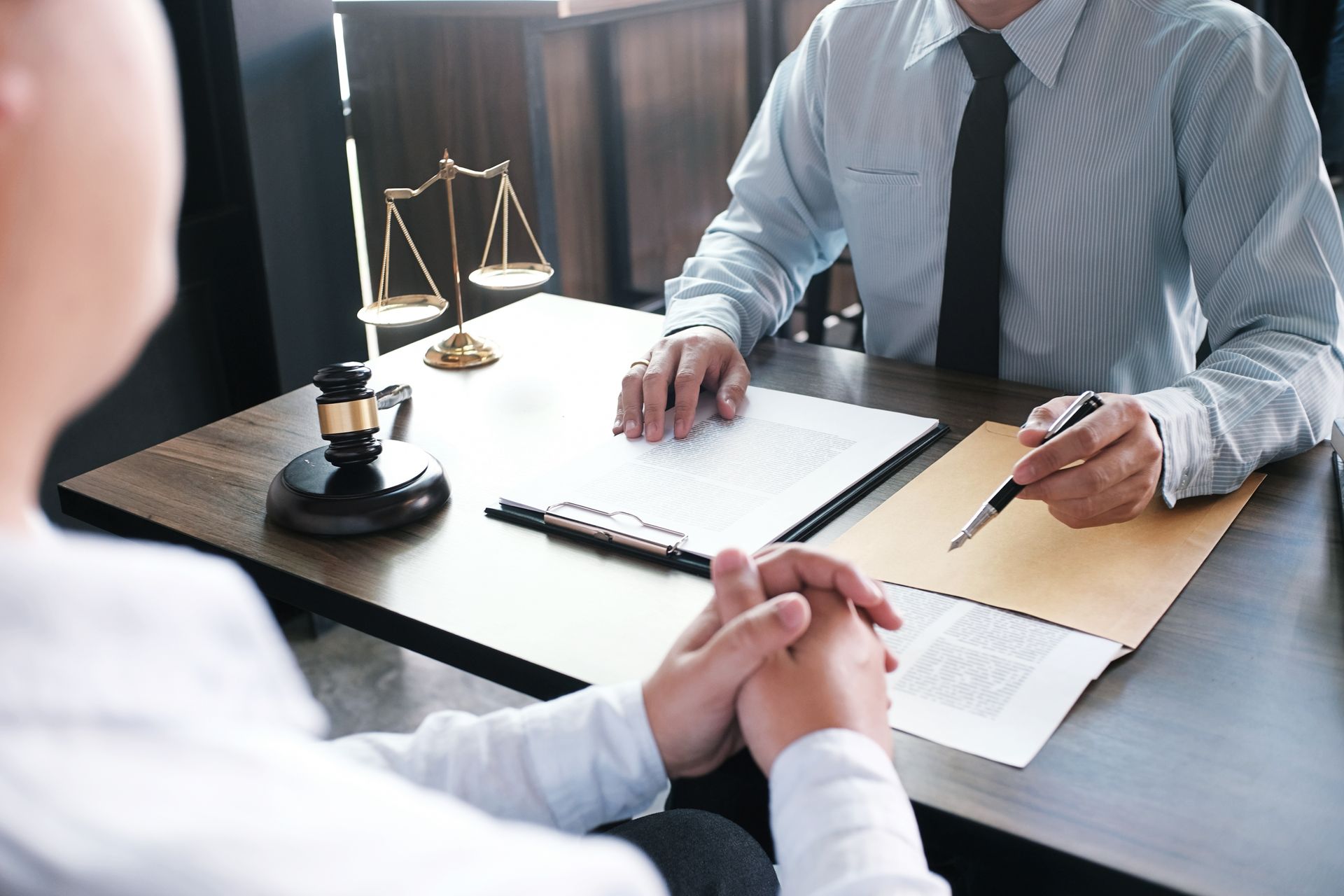 Attorney meeting with client at desk, reviewing documents with a scale of justice nearby.
