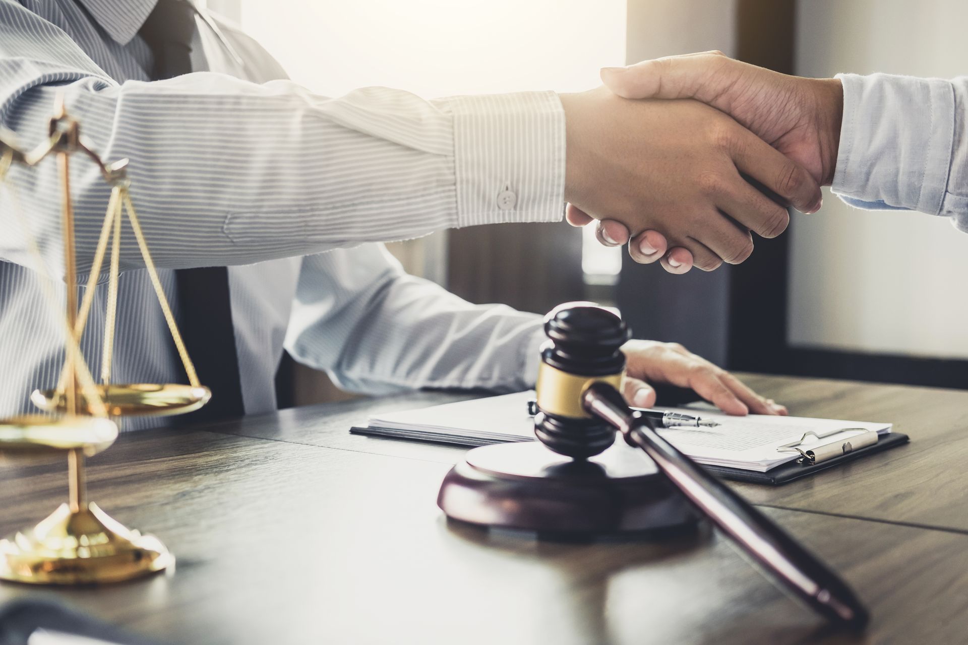 Handshake over a desk with a gavel and scales of justice, suggesting a legal agreement