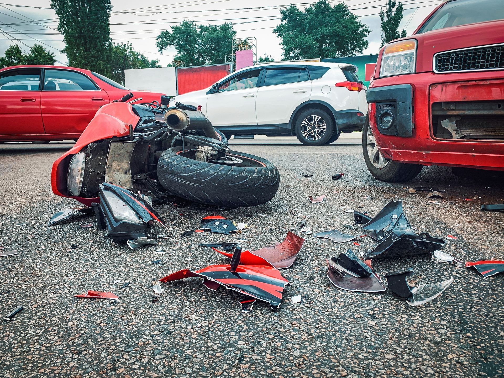 Motorcycle wreck with debris on a road, with a red car and white SUV nearby