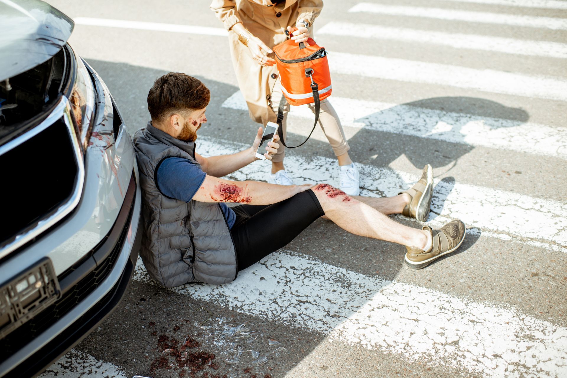 Man sitting on a zebra crossing with a service dog in an orange vest beside him