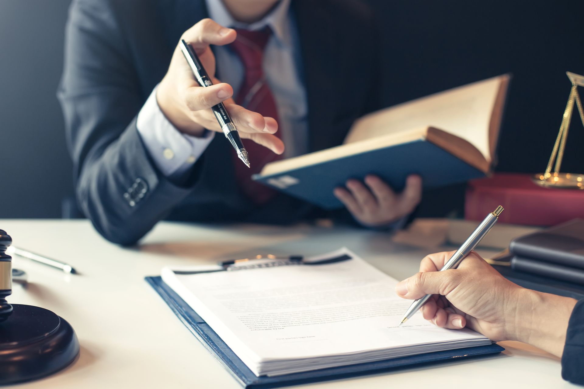 Business meeting with two people signing documents at a desk, holding a pen and open book