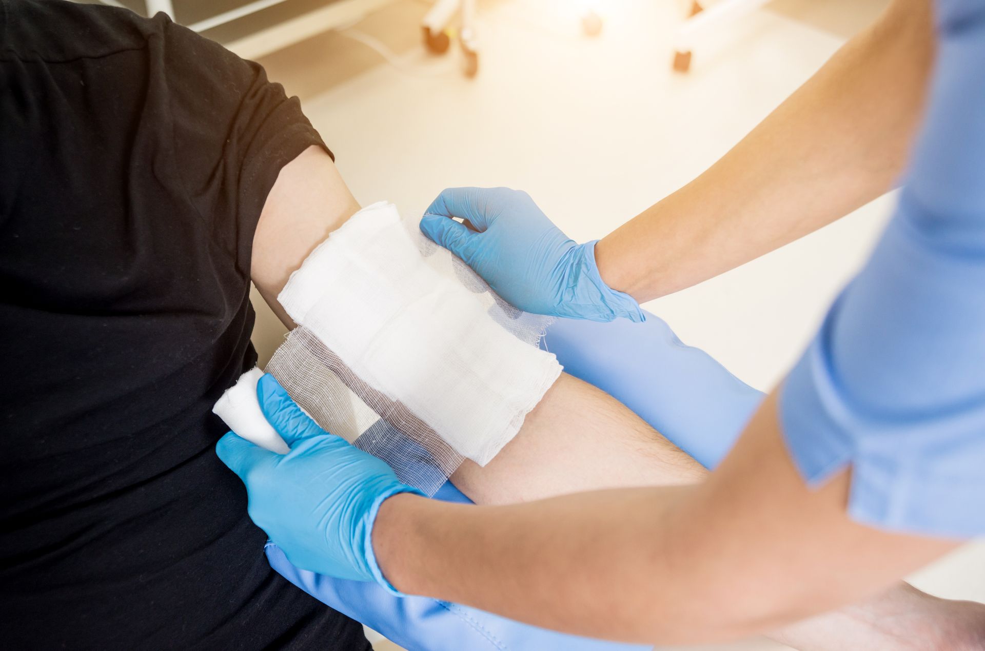 Healthcare worker bandaging a patient’s arm with blue gloves in a clinic setting