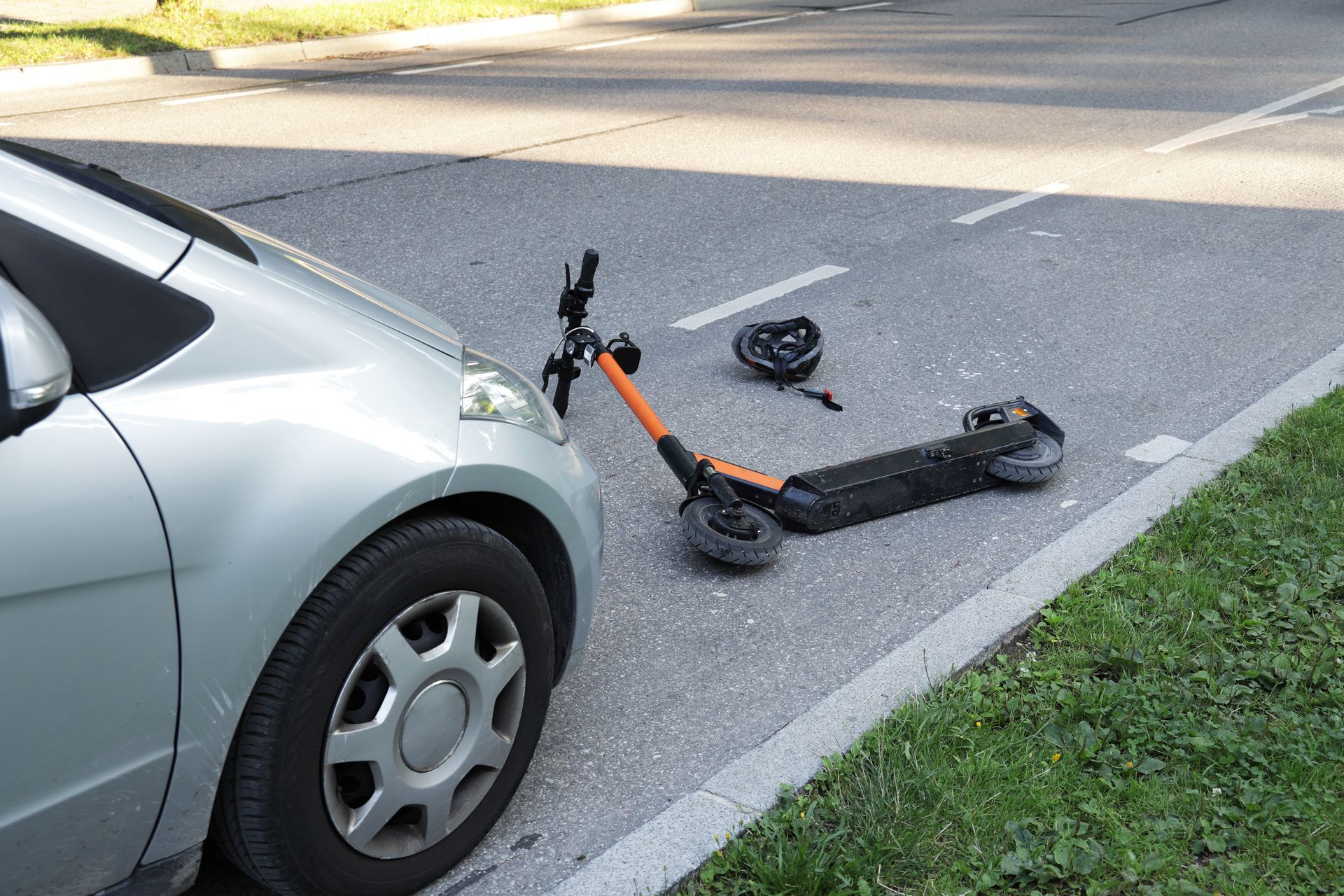 Silver car next to a fallen black-and-orange scooter on the roadside