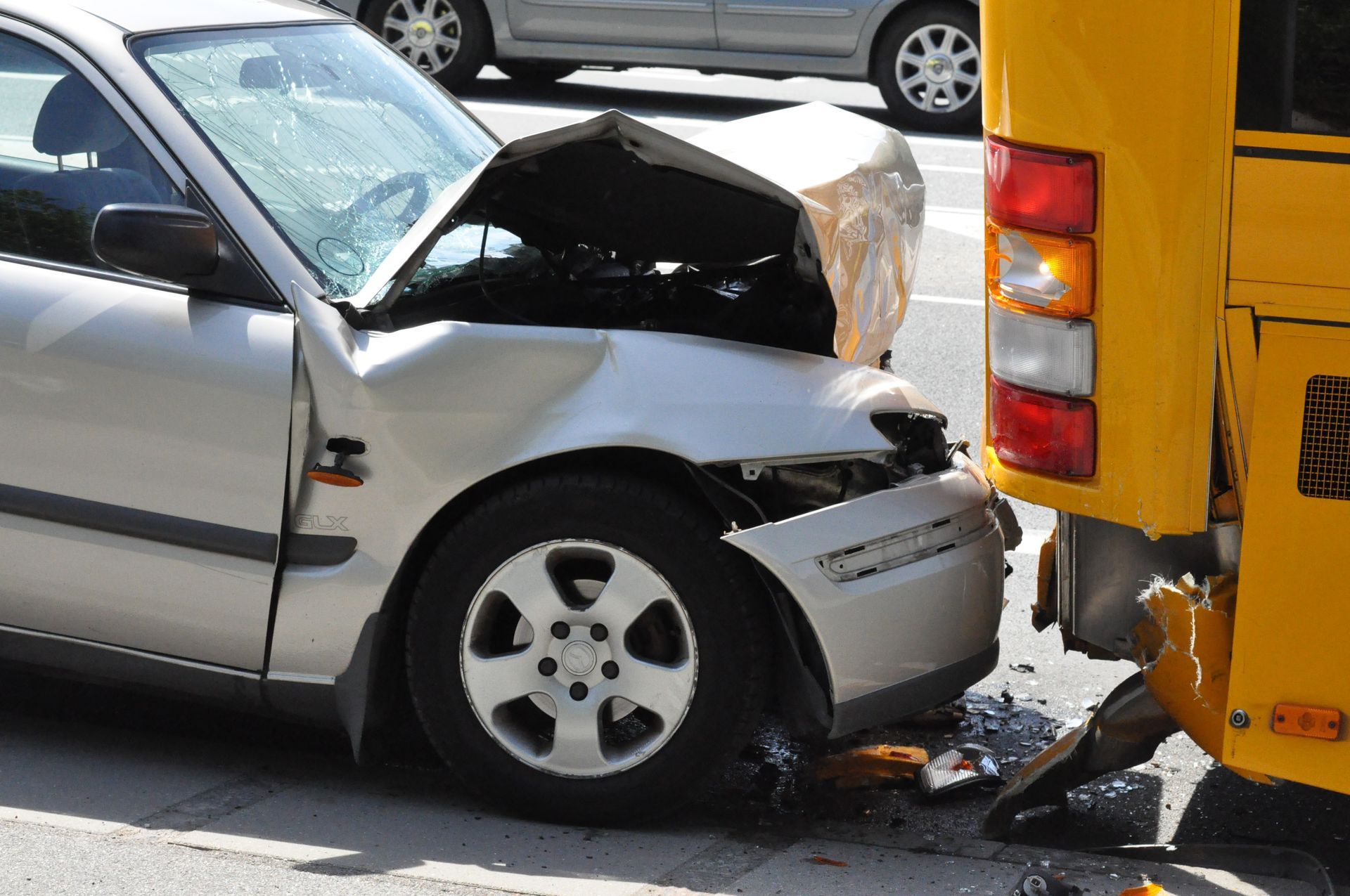 Silver car with crushed front end rear-ended by a yellow bus on a road