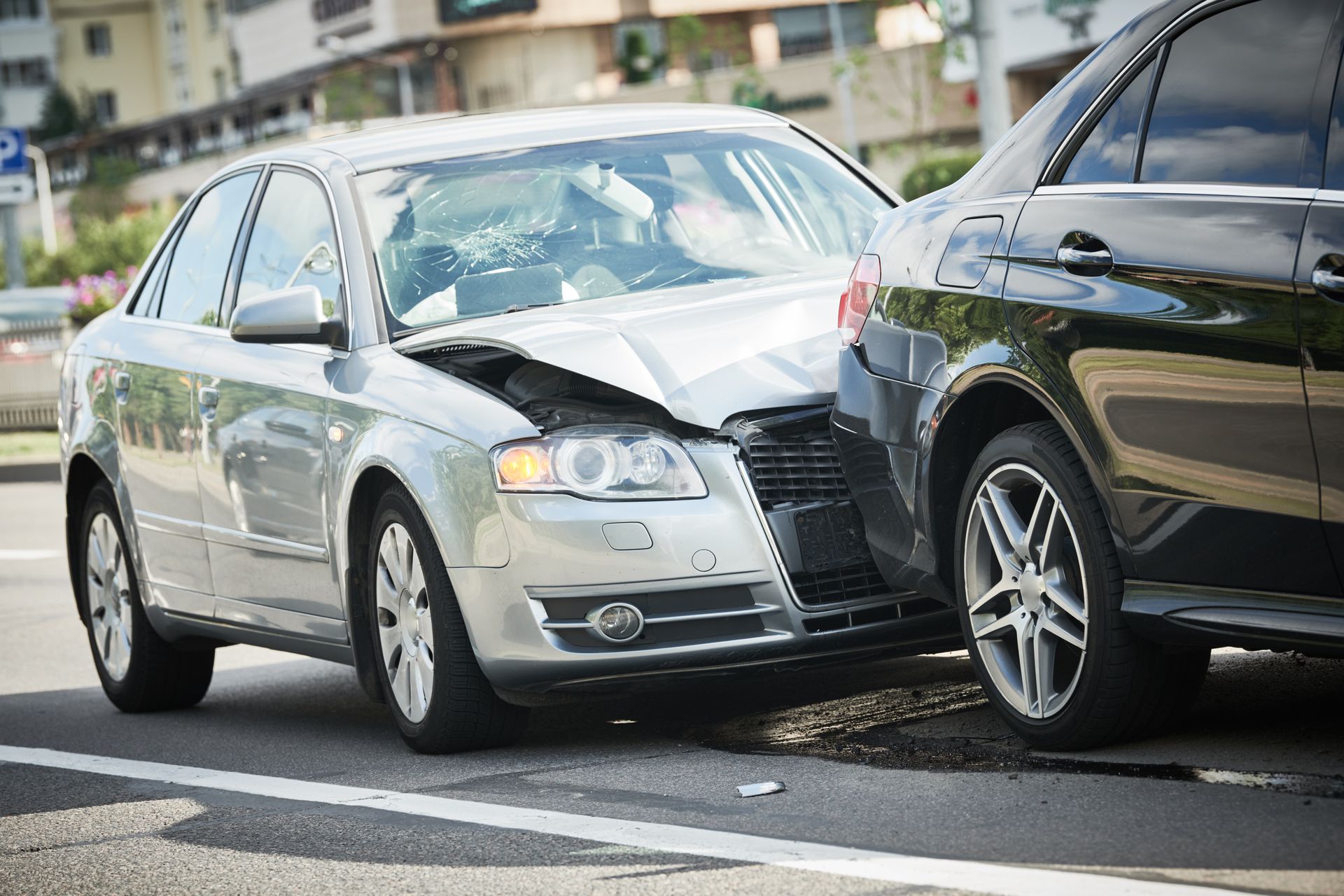 Silver sedan with front-end damage stopped behind a black car on a city street