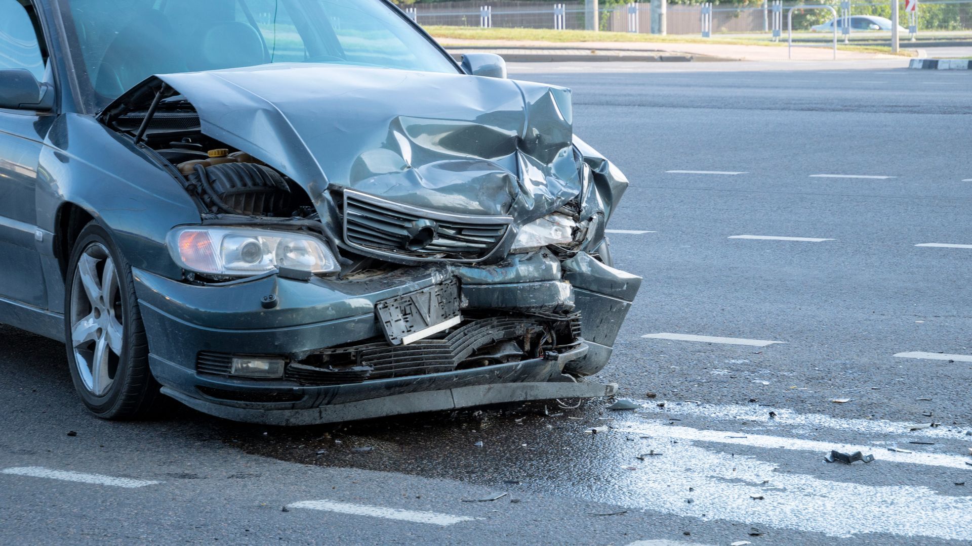 Damaged blue car with crushed front end at a roadside collision scene