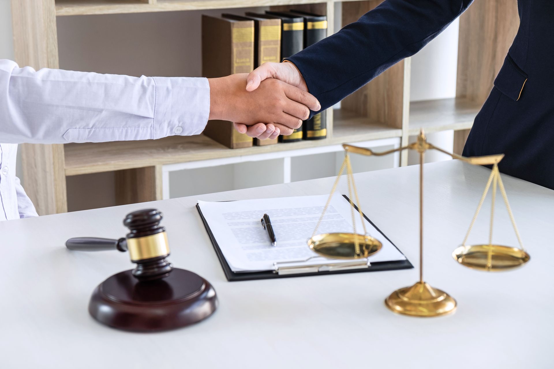 Handshake over a lawyer’s desk with scales of justice, gavel, and legal documents