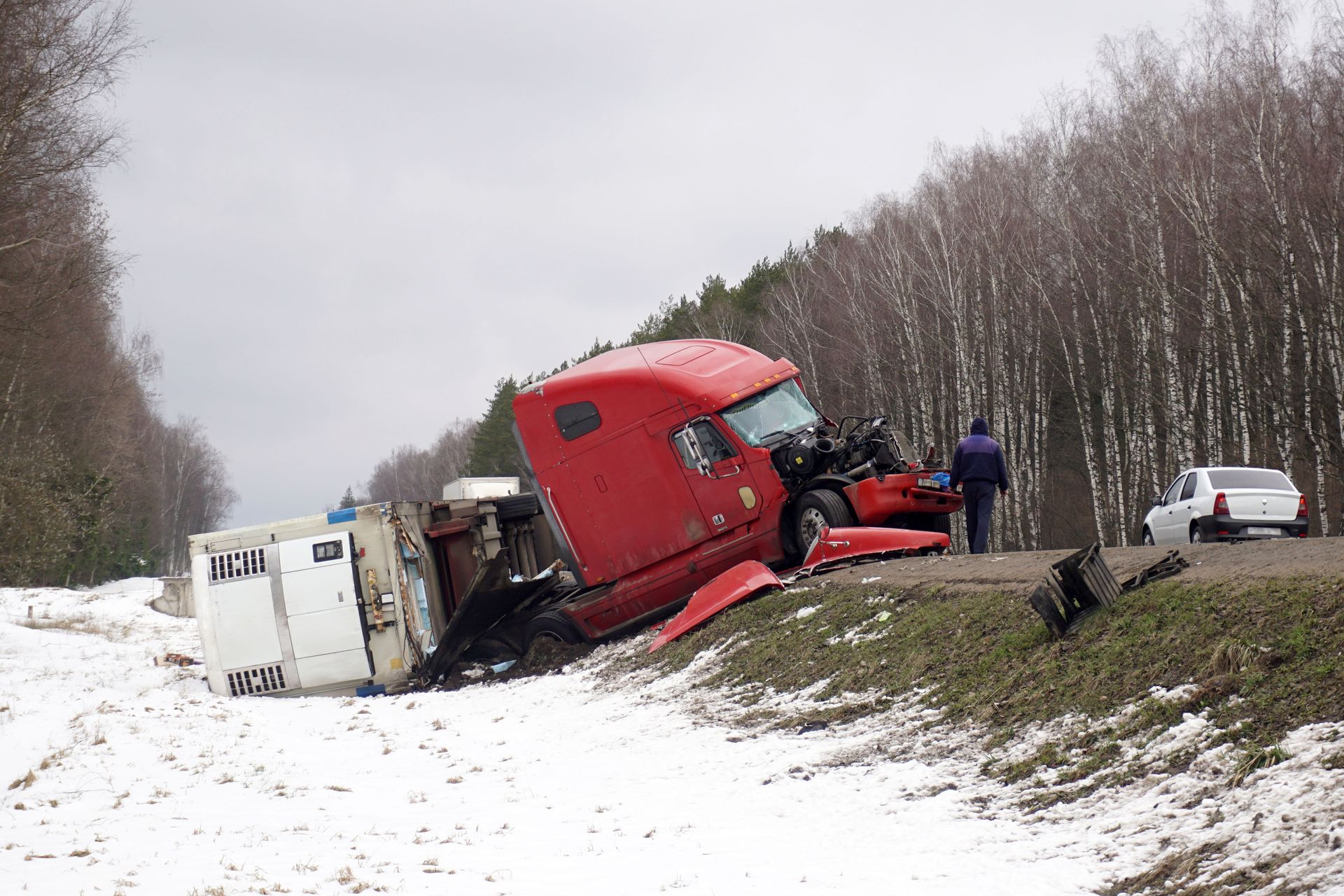 Red semi-truck rear-ended a silver SUV on a roadside in a forested area.