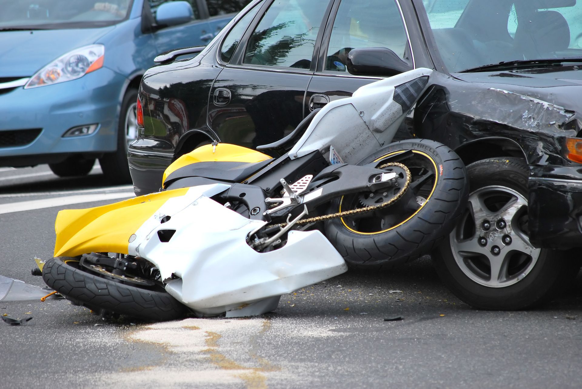 Yellow and white motorcycle crashed into a black car on a street, with front-end damage visible.