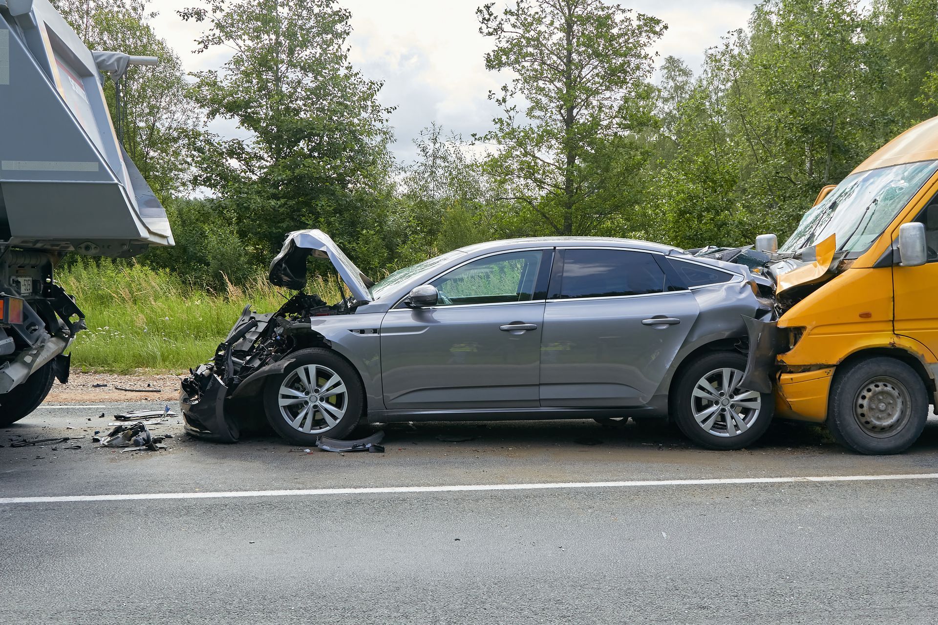 Gray sedan with crushed front end after a collision with a yellow truck on a roadside.