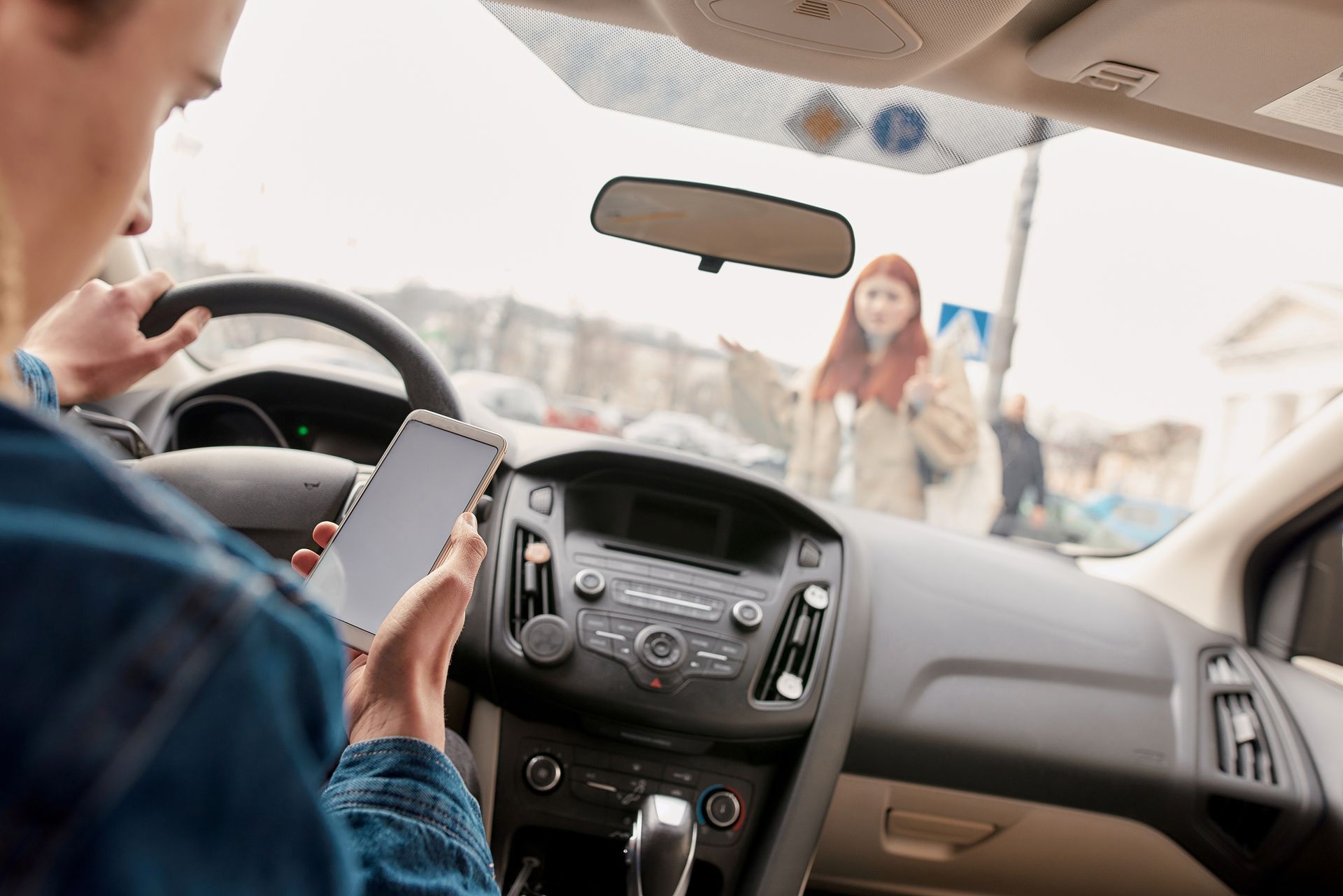 Driver texting while a person stands in front of the car on a snowy street