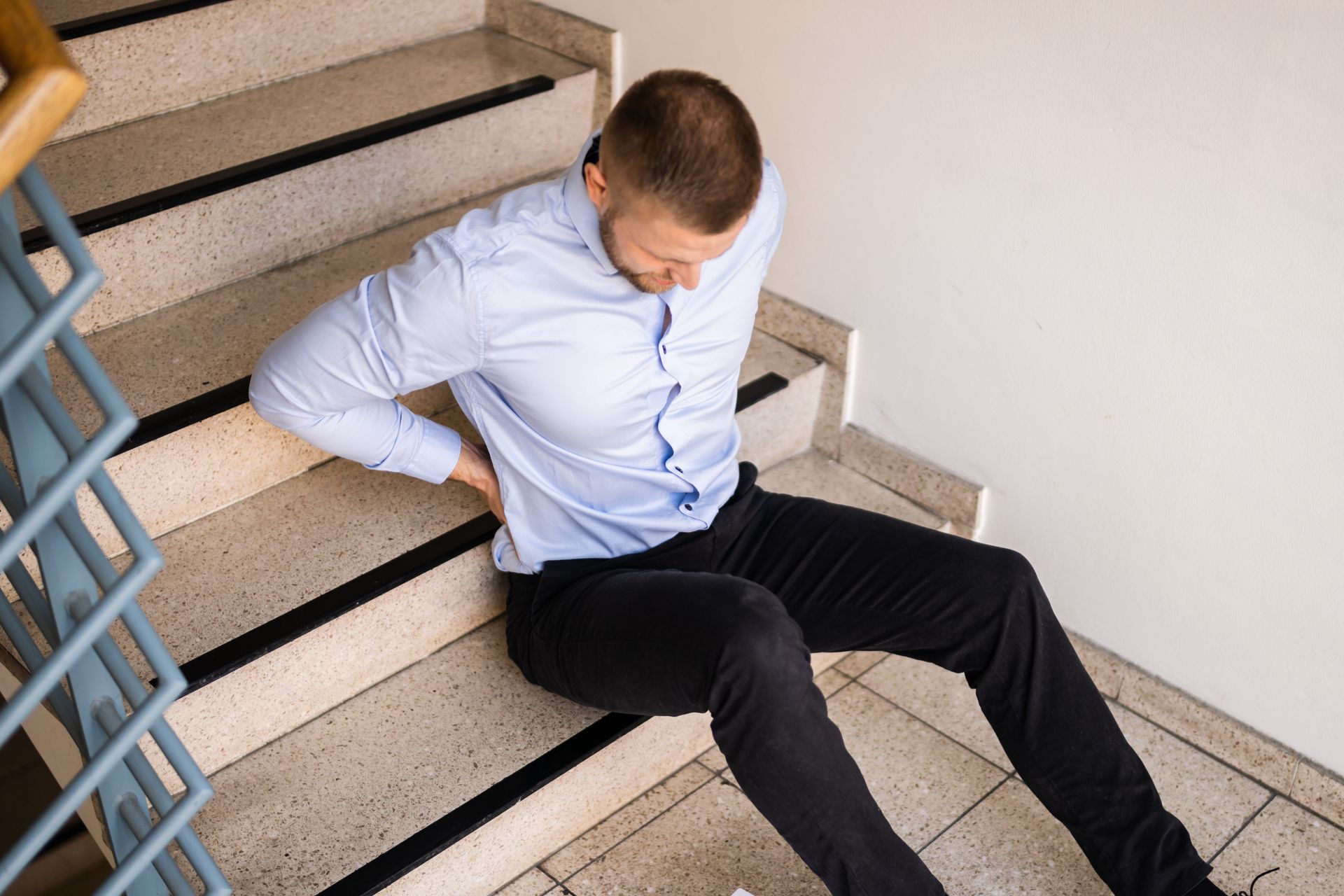 Man sitting on stairs with back pain, leaning against the steps in a stairwell