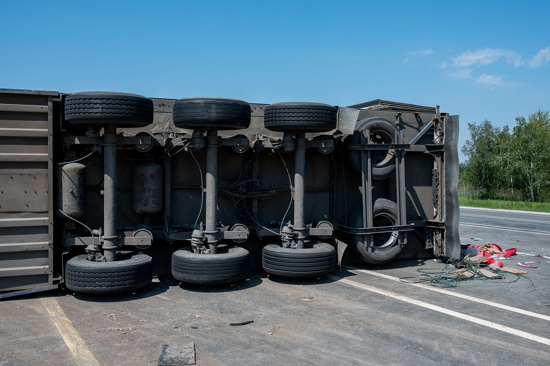 Overturned truck on roadside, tires exposed, with debris scattered on a sunny day