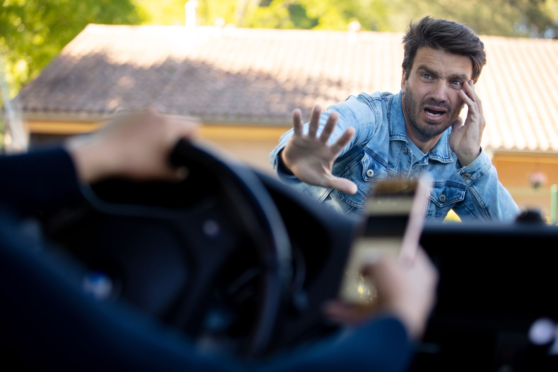 Driver’s view of a man in a blue shirt shouting and reaching toward the car window outside