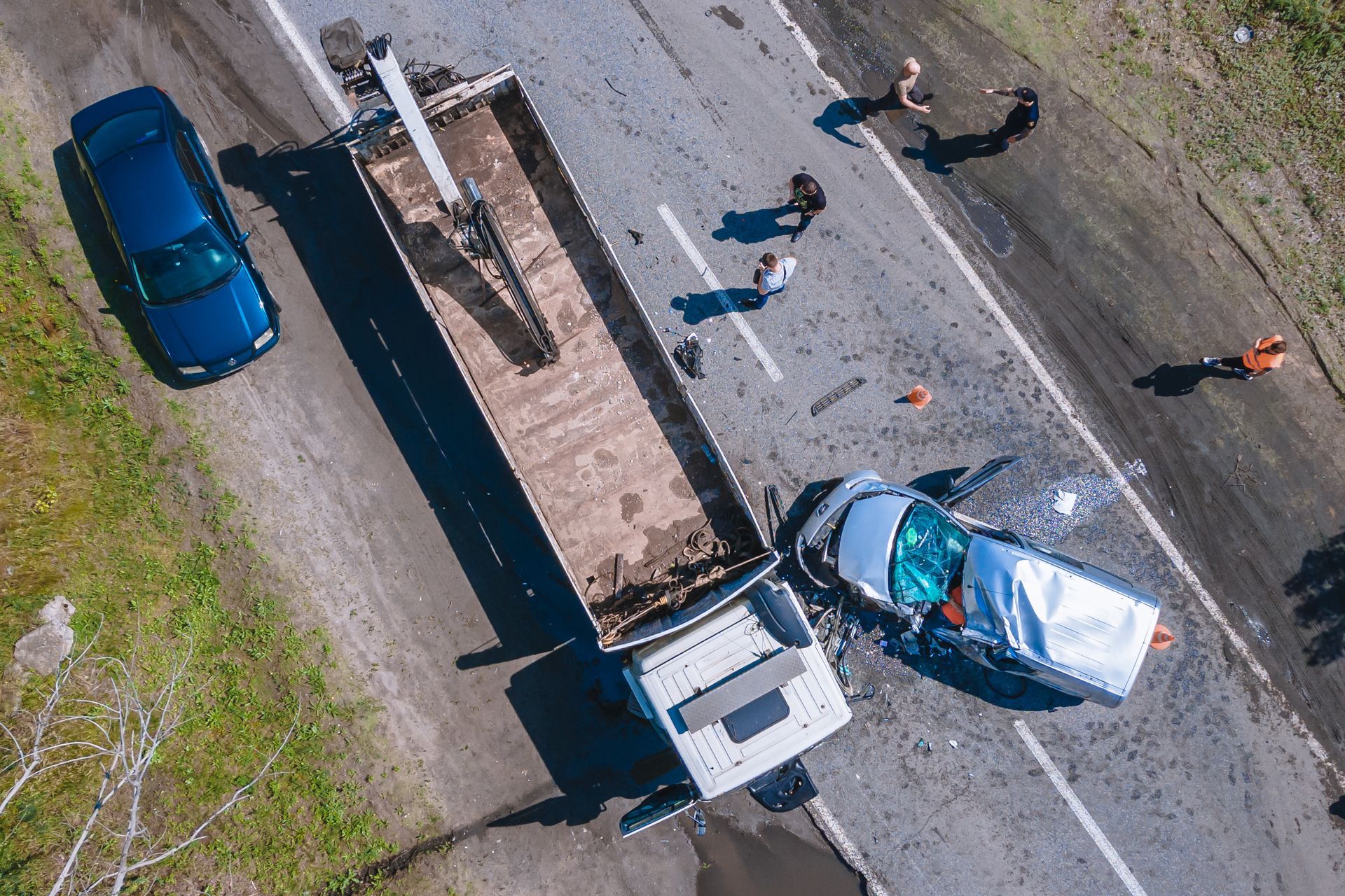 Aerial view of a truck and damaged car at a roadside crash scene with several people nearby.