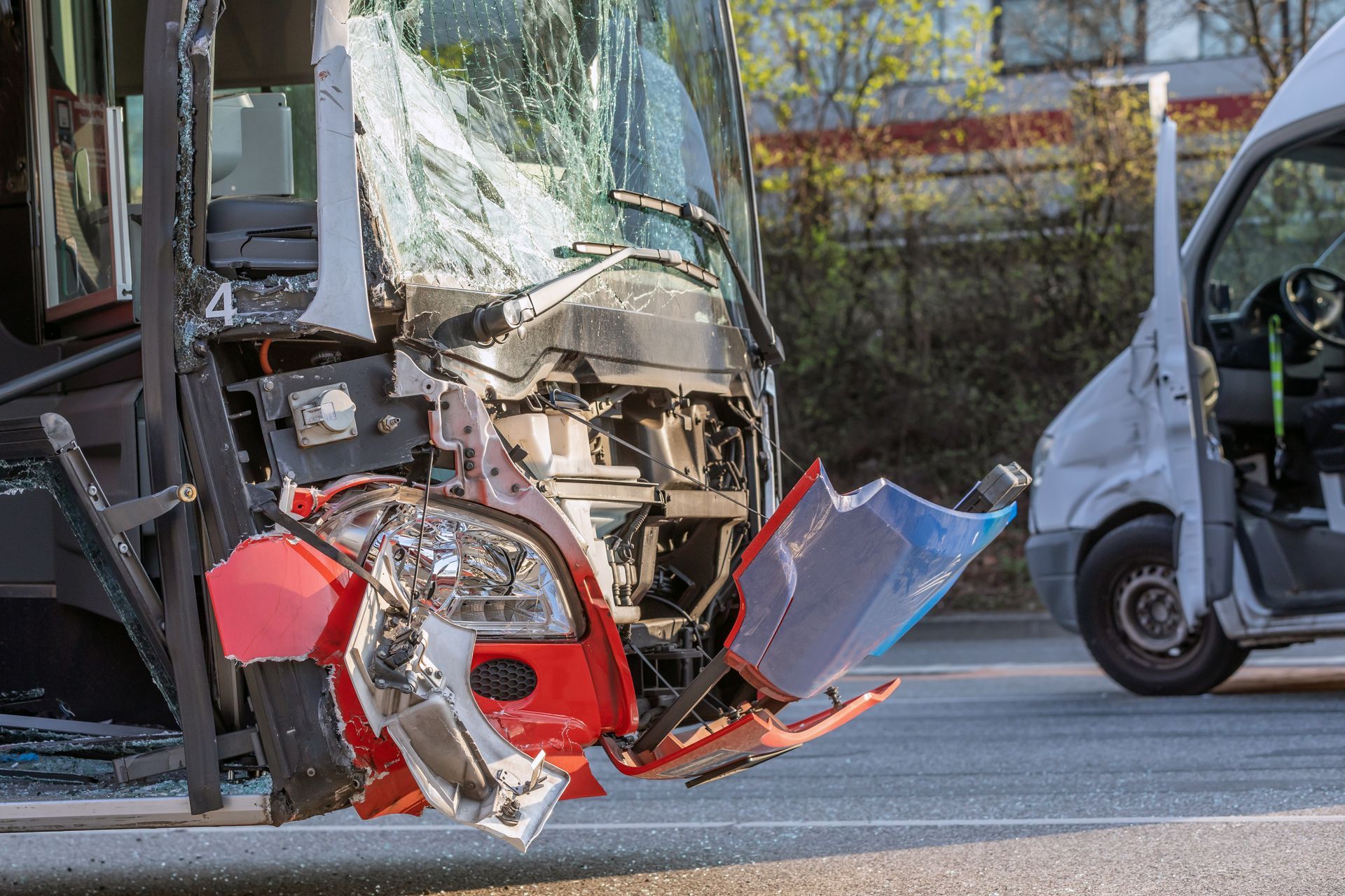 Damaged bus after a crash, with debris scattered on the street and a van in the background