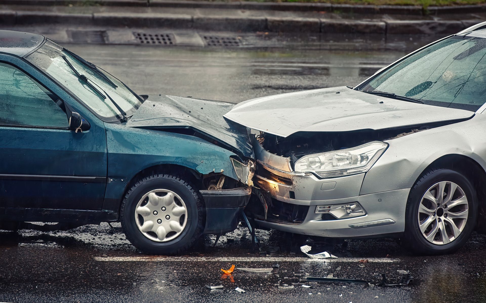 Two cars with front-end collision on a wet road, one dark blue and one silver.