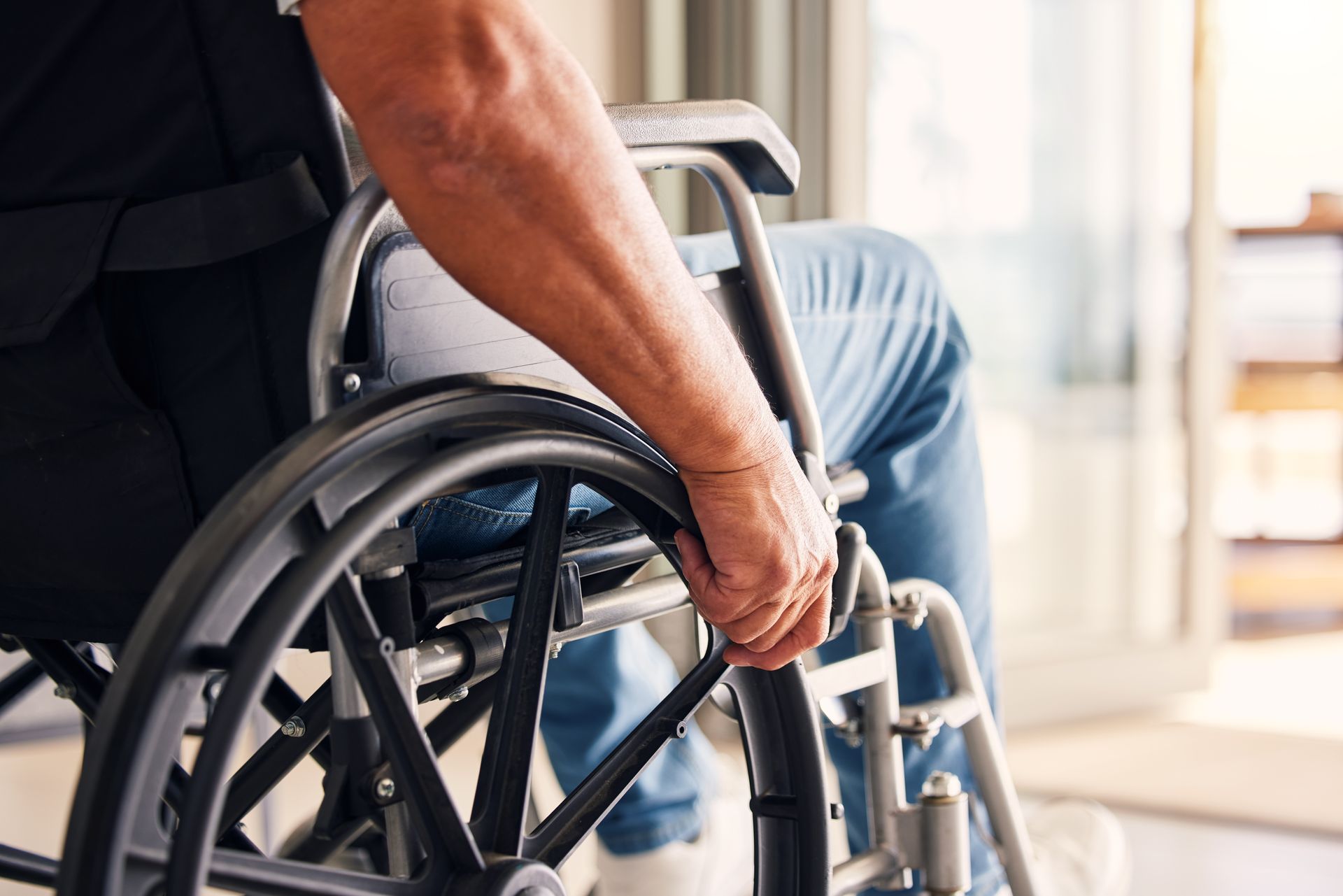Person in a wheelchair being pushed indoors, with a caregiver’s hand on the wheel