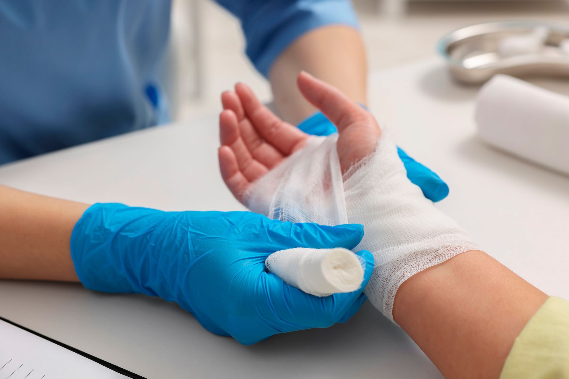 Gloved hands bandage a patient’s wrist on a clinic table