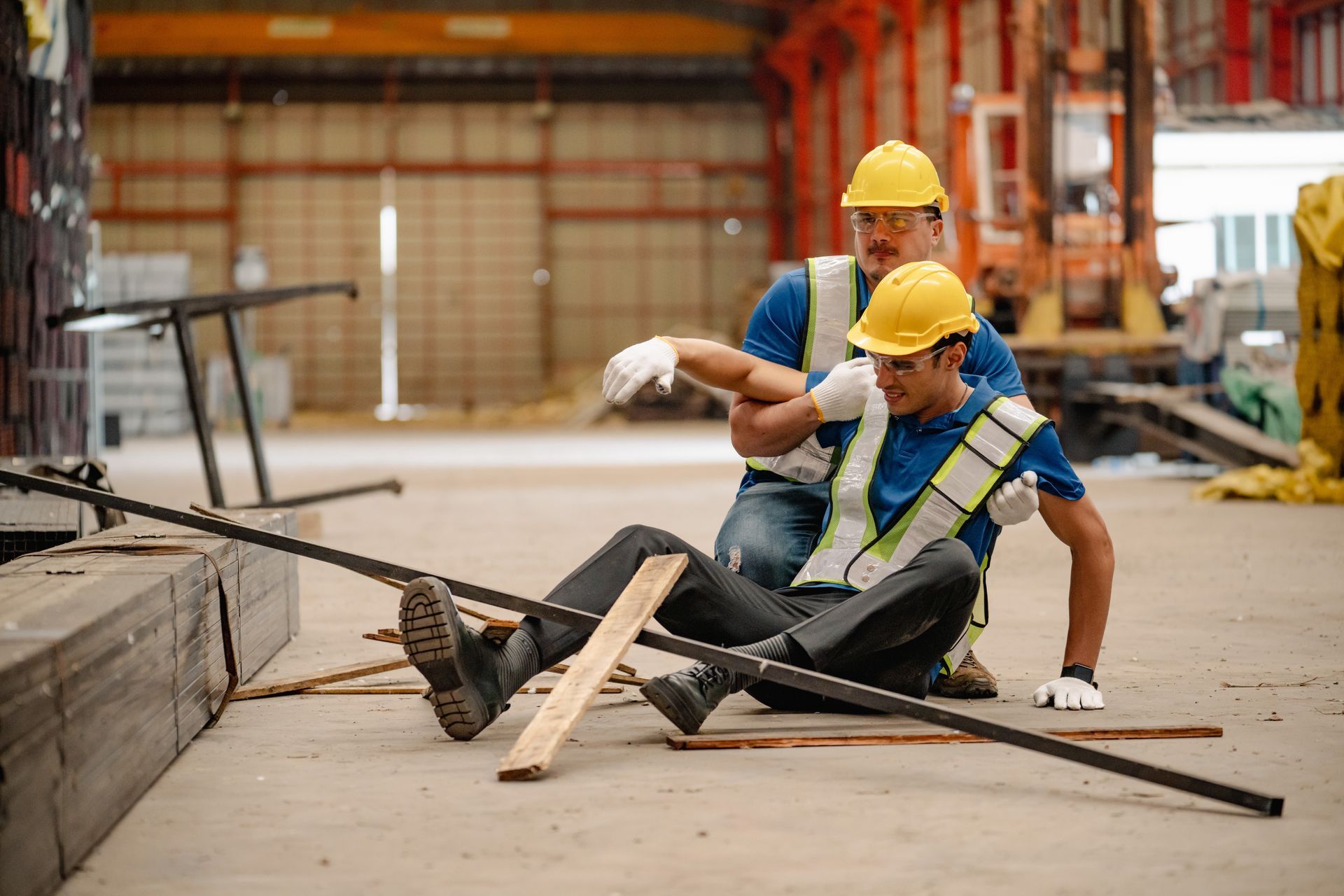 Yellow hard hat with tools in foreground; blurred construction workers kneel at a building site.
