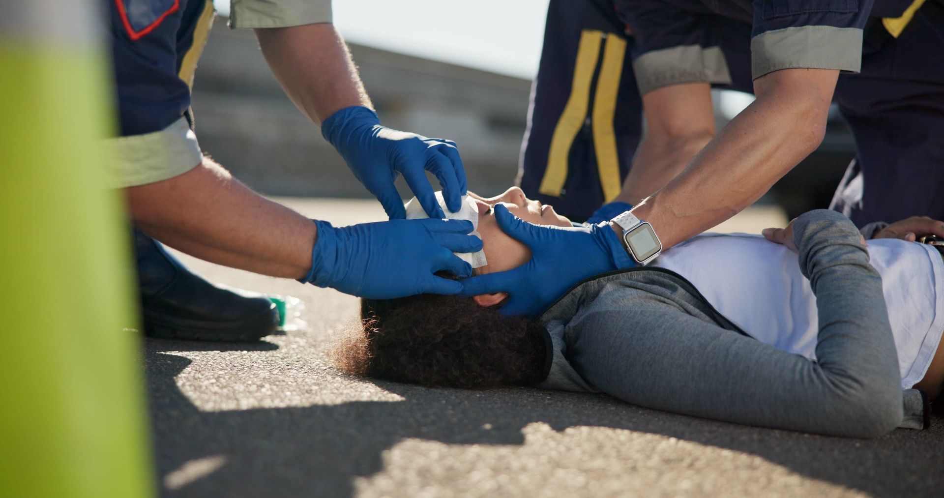 Paramedics in blue gloves treating an injured person lying on a road