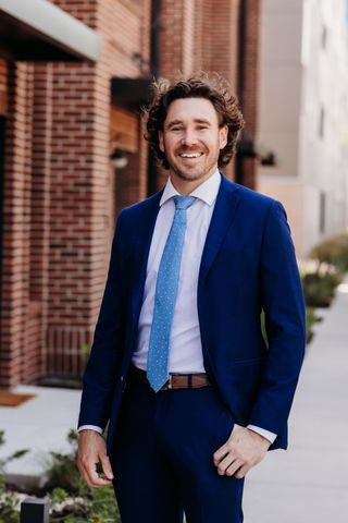 Smiling man in a suit and blue tie standing in a doorway