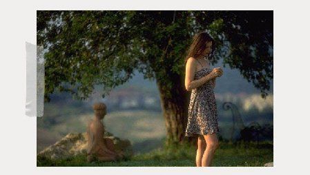 A woman in a dress is standing next to a tree.