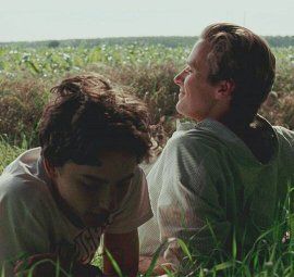 Two men are sitting in the grass in a field.
