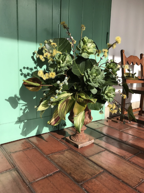 A vase filled with flowers sits on a tiled floor in front of a green door.