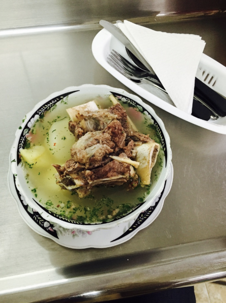 A bowl of soup with meat and potatoes on a table