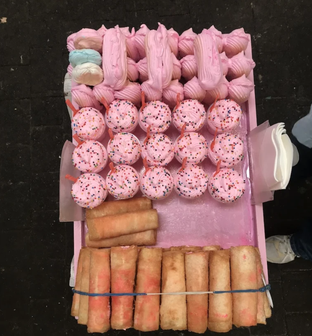 A pink tray filled with pink cupcakes and rolls