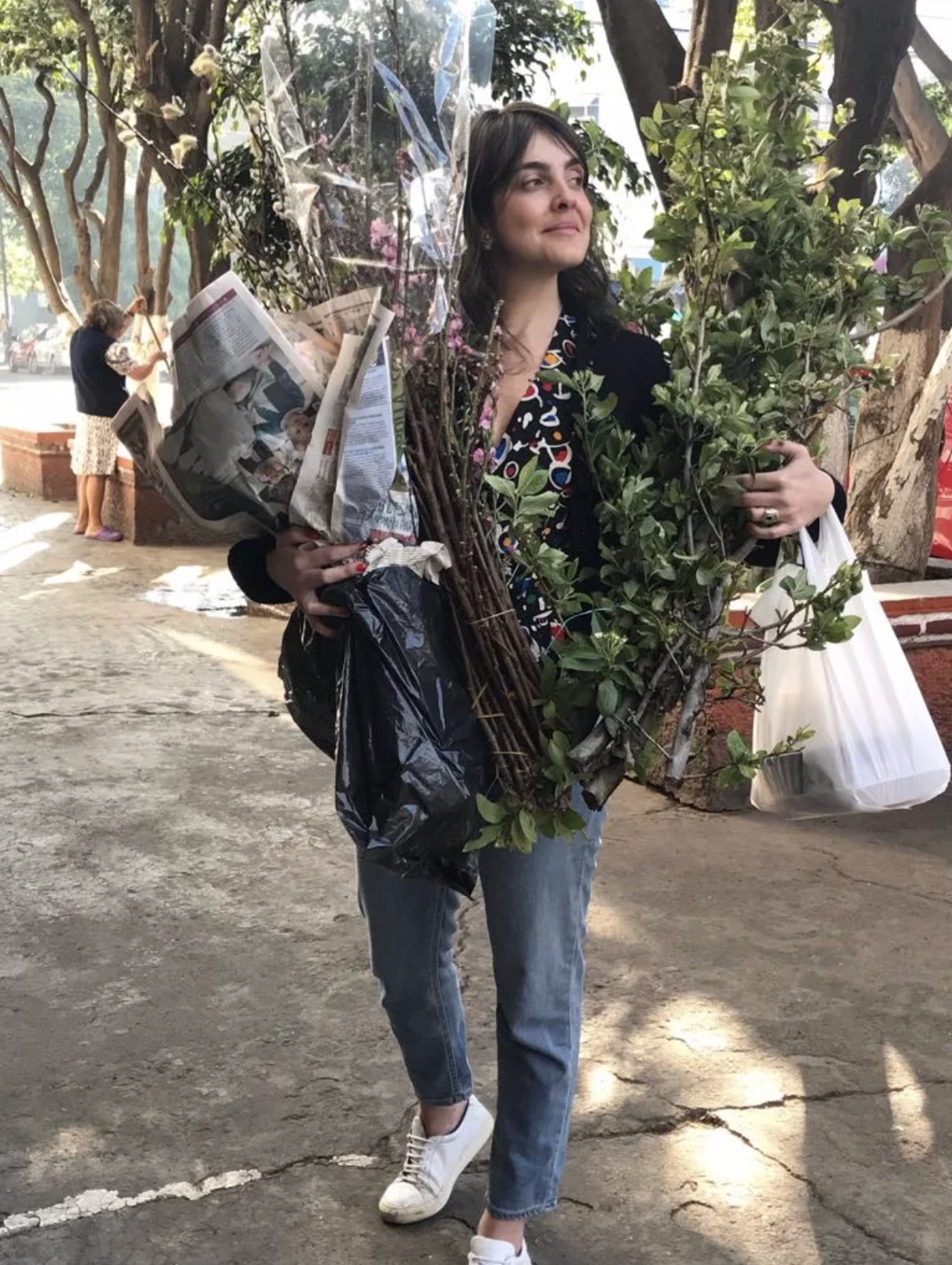 A woman is carrying a large bouquet of flowers and newspapers.
