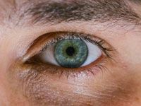 Close-up of a green eye with a dark pupil and visible eyelashes, framed by the surrounding skin.