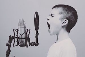Child singing into a studio microphone with a pop filter, mouth open in a recording setup