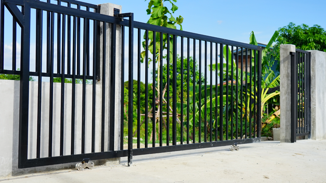Modern balcony railing with horizontal steel cables and dark metal posts, against a white building and palm trees.