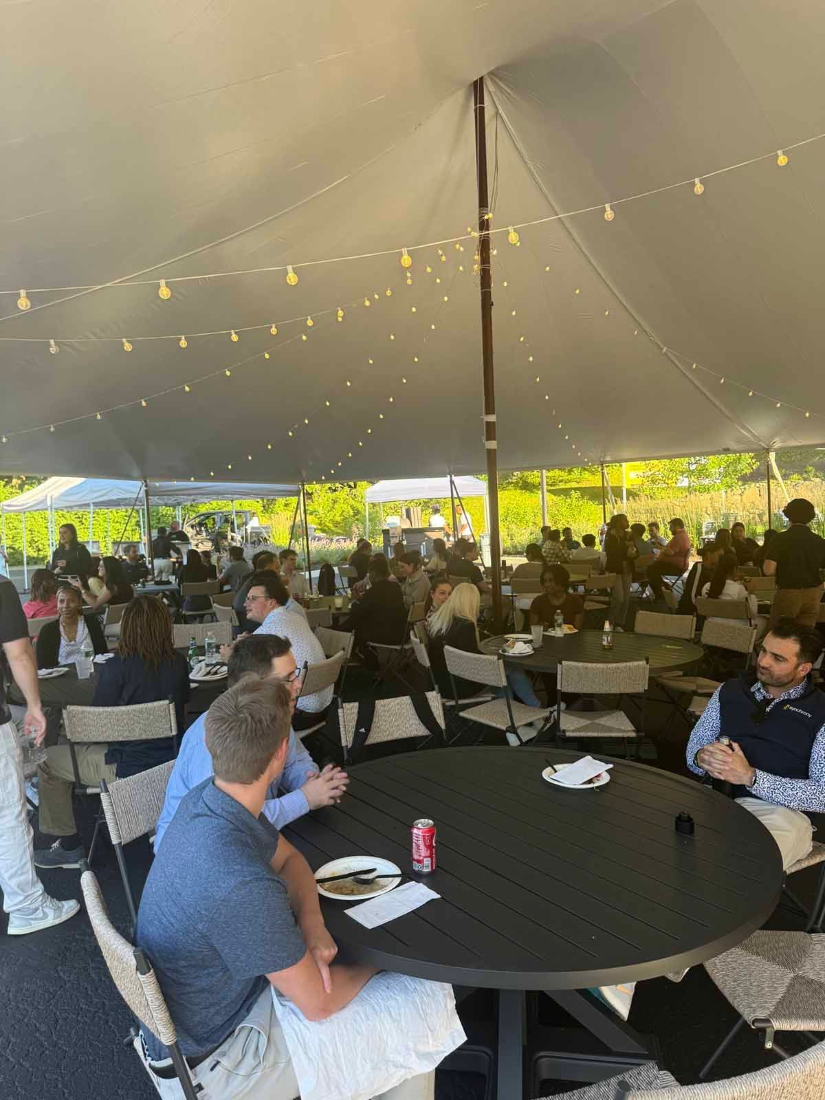 A group of people are sitting at tables under a tent.